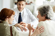 © PhotoAlto - Woman talking with her mother, doctor looking at them in clinic