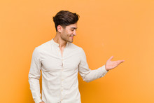 Young Handsome Man Feeling Happy And Cheerful, Smiling And Welcoming You, Inviting You In With A Friendly Gesture Against Orange Background