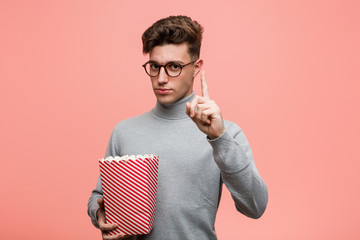 Wall Mural - Young intellectual man holding a popcorn bucket showing number two with fingers.