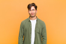 Young Handsome Man Looking Goofy And Funny With A Silly Cross-eyed Expression, Joking And Fooling Around Against Orange Background