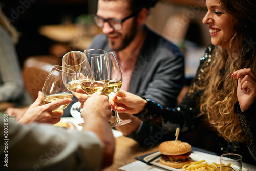 Fotografía Best friends sitting in restaurant for dinner and making a toast with white wine