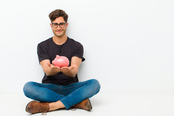 Wall Mural - young handsome man with a piggy bank sitting on the floor sitting on the floor in a white room