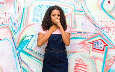 young pretty african american woman feeling ill with a sore throat and flu symptoms, coughing with mouth covered against graffiti wall