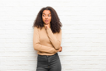 Wall Mural - young black woman smiling happily and daydreaming or doubting, looking to the side against brick wall