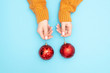 Beautiful female hands in warm knitted sweater holding New Year red balls to decorate Christmas tree blue background. Top view