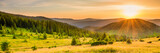 Fototapeta  - Panorama of sunset in the mountains with forest, green grass and big shining sun on dramatic sky