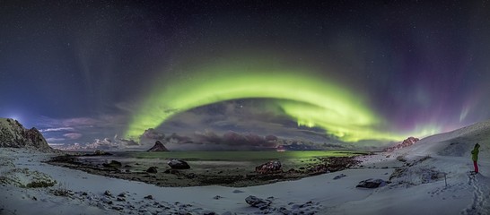 Wall Mural - Wide shot of a the snow covered shore by a lake under the northern lights in the sky in Norway