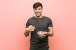 © Asier - Young hispanic man holding a cereal bowl surprised pointing at himself, smiling broadly.