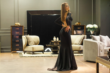 Wall Mural - Sexy blonde woman in a black evening dress posing in a furniture store