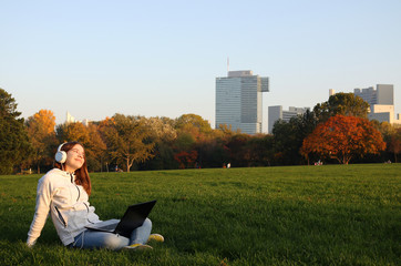 Wall Mural - happy teenage girl is listening to music on a laptop and enjoying in park