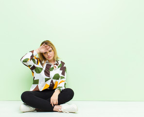 Wall Mural - young blonde woman looking stressed, tired and frustrated, drying sweat off forehead, feeling hopeless and exhausted sitting on the floor