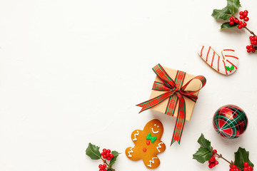 Christmas background with gingerbread cookies, gift boxes and branches of holly with red berries on white. Winter festive nature concept. Flat lay, copy space.