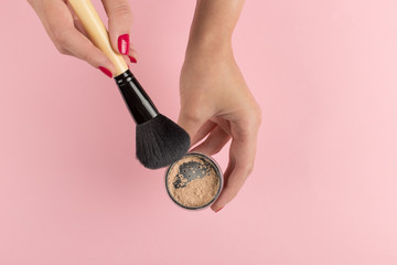 Wall Mural - Girl's hands hold powder and makeup brush on a pink background, copy space.