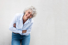 Older Woman Laughing With Arms Crossed By Gray Wall