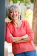 beautiful older woman leaning against wall smiling with arms crossed outdoors