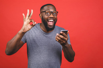 Afro american man using smartphone over isolated red background doing ok sign with fingers, excellent symbol.