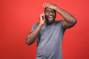 Portrait of a happy african american guy talking on mobile phone isolated against red background.