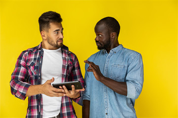 afroamerican guy is proving smth to european guy  in informal shirts on the yellow background