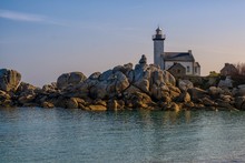 White Lighthouse Near Rock Formations On The Shore Of The Sea
