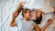 Guy and a girl in a cozy home environment. Happy man and woman lying in the bedroom stock photo. Top view of smiling young couple cuddling in bed in morning.  Beautiful pair of lovers hug and kiss