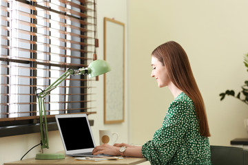 Wall Mural - Young woman using laptop at table indoors. Space for text