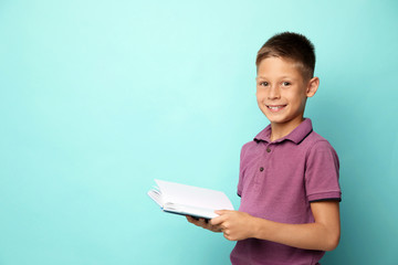 Wall Mural - Portrait of cute little boy reading book on turquoise background. Space for text