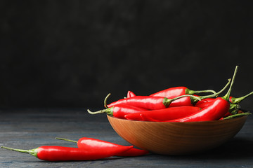 Bowl with red hot chili peppers on wooden table against black background. Space for text