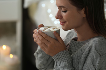 Canvas Print - Young woman holding cup of hot cocoa with marshmallows at home. Cozy winter