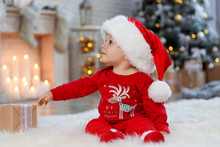 Little Baby With Santa Hat And Christmas Gift On Floor At Home