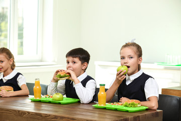 Happy children eating healthy food for lunch in school canteen