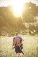 Sticker - Vertical shot of a male walking in a field next to a forest with a guitar on his back