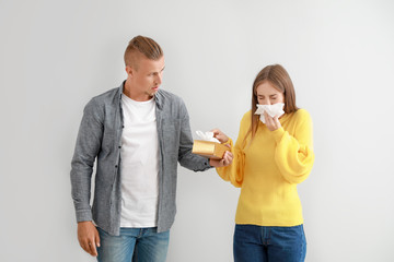 Wall Mural - Young man giving to woman suffering from allergy nose wipers against light background