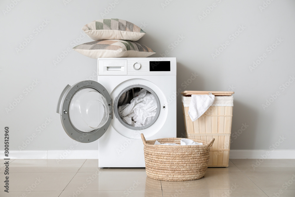 Modern washing machine with laundry near white wall - obrazy, fototapety, plakaty 