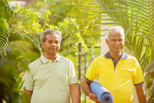 Happy Senior People With Yoga Mat In Park - Healthy Elderly Men With Fitness Mat Outdoor - Older Joyful Friends Walking In Garden During Morning.