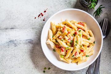 Wall Mural - Penne pasta with chicken, pepper and green onions in creamy sauce in a white plate, gray background, top view.