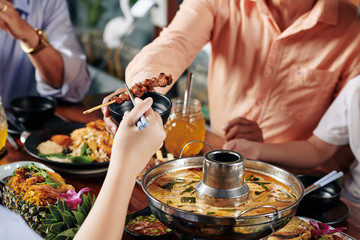 Poster - Hand of child taking delicious skewers with chopsticks when sitting at dinner table with relatives