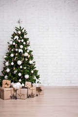 christmas and new year background - christmas tree and gift boxes over white brick wall with copy sp
