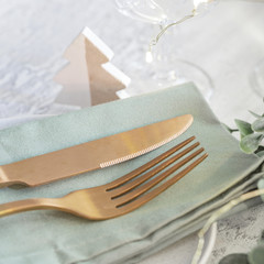 Wall Mural - Nordic Festive tableware for Christmas and New Year celebration. Close up  of Gold cutlery and green linen napkin on cement background. Kinfolk style