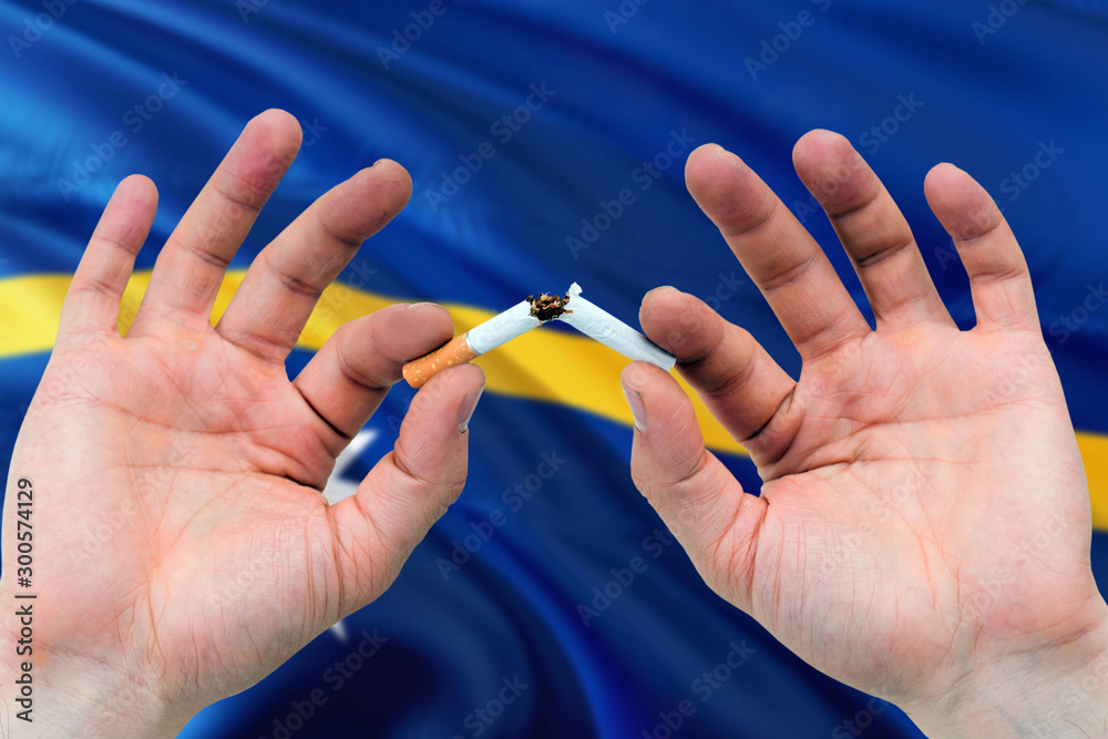 nauru cigarette addiction Nauru quit smoking cigarettes concept. Adult man hands breaking cigarette.  National health theme and country flag background. Stock Photo