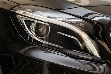 Wall Mural - Front headlamp view of black used car stands in the auto showroom sale after washing and polish with orange turn light and bi-xenon lens