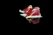 studio photo of a series of slices of 100% Iberian acorn-fed ham folded on black background with reflection