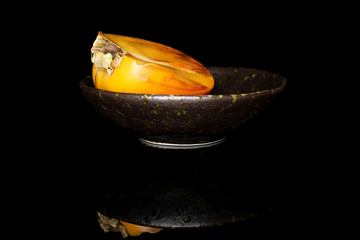 Wall Mural - One half of sweet orange persimmon in glazed bowl isolated on black glass