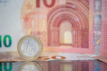 Macro photo of a coin in 1 euro on a blurred background banknote in ten euro. Reflection of the coin on the glass table. Very small depth of field.