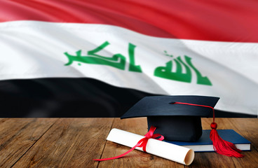 Iraq education concept. Graduation cap and diploma on wooden table, national flag background. Succesful student.