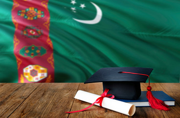 Turkmenistan education concept. Graduation cap and diploma on wooden table, national flag background. Succesful student.