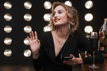 Canvas Print - Image of fancy blonde woman using cellphone and drinking red wine in bar