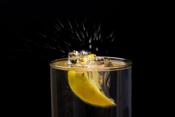 Limón entrando en un vaso o jarro de cristal transparente lleno de agua, chapoteo, agua salpicando y saliendo del vaso