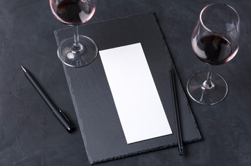 Wine tasting table. Pair of wineglasses, empty paper, pen, slate placemat on the black table