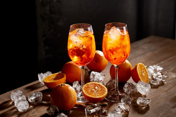 Wall Mural - Aperol Spritz in glasses, oranges and ice cubes on black background