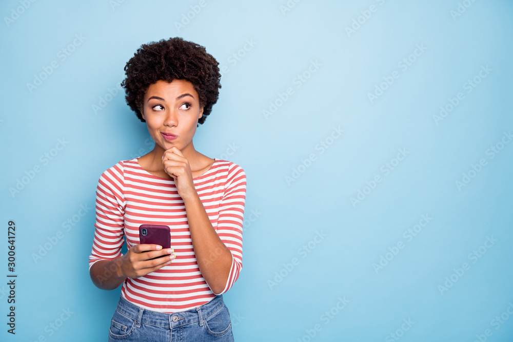 Photo of wondered interested thinking youngster holding telephone puzzled about what message to send looking for ideas in empty space in striped shirt isolated pastel color background - obrazy, fototapety, plakaty 